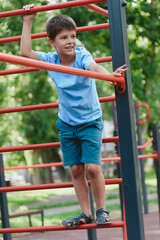Obraz premium Happy boy playing and hanging on steel bar on playground. Children's exercises for health and concentration.