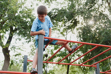 Happy boy playing and hanging on steel bar on playground. Children's exercises for health and concentration.