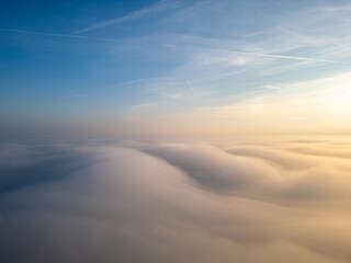Rolling Clouds Beneath a Golden Sky. A serene aerial view of soft, rolling clouds illuminated by the warm hues of a golden sky, with contrails stretching across the tranquil blue horizon.