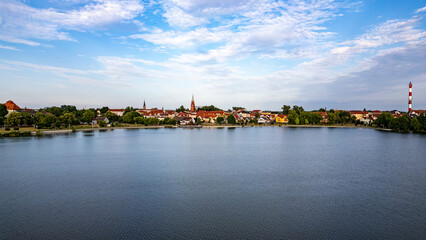 Obraz premium Serene View of Lake Raduń in Wałcz, Poland. Calm waters of Lake Raduń surrounded by vibrant architecture and lush greenery under a clear blue sky