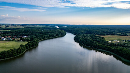 Meandering Lake Raduń Surrounded by Forests in Wałcz, Poland. erial view of Lake Raduń winding through lush forests and rural landscapes, reflecting the calm sky