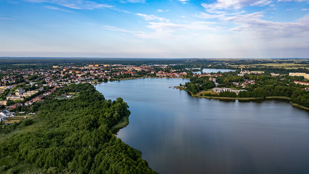 Panoramic View of Lake Raduń in Wałcz, Poland. Aerial view of Lake Raduń in Wałcz, Poland, surrounded by lush greenery, urban architecture, and a serene water surface reflecting the clear blue sky.