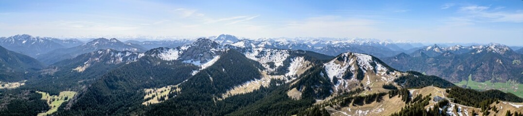 Panoramic aerial view of the foothills of the Alps in Bavaria. Edge of mountains, sky and clouds. The mountains are covered with snow and forests.