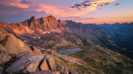 Fototapeta premium The sun sets behind a mountain range, spreading vibrant colors across the sky, while shadows deepen on the rugged terrain below