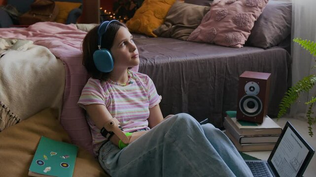 Zoom in view of gen alpha girl with disability listening to music with headphones and holding smartphone while sitting on floor next to laptop
