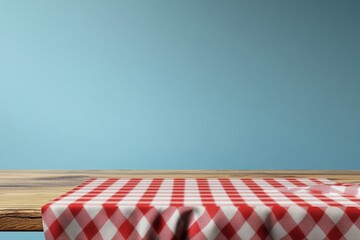 Empty wooden table with red checkered tablecloth against a light blue wall.