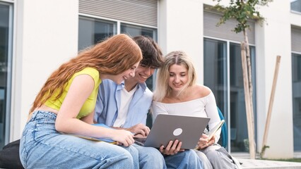 Fototapeta premium Smiling young friends using laptop outside university building