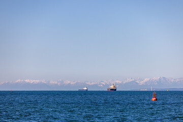 Fototapeta premium Cargo Ships Anchored in Open Ocean with Snowy Mountains in the Background