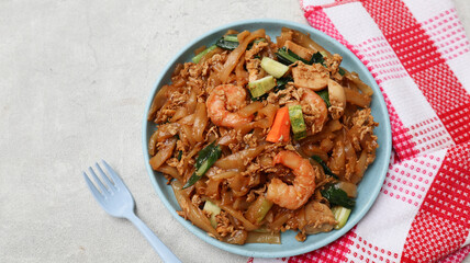 Kwetiaw or Kwetiau seafood, fried rice noodles with prawn or shrimp and vegetables. Popular in Indonesia served on blue plate isolated on grey