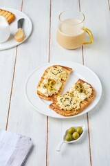 Healthy breakfast, two open sandwiches with hummus, egg salad and olives on white plate on light wooden background. Healthy food.