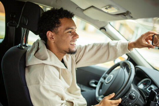 Man adjusting rear view mirror in a car, smiling