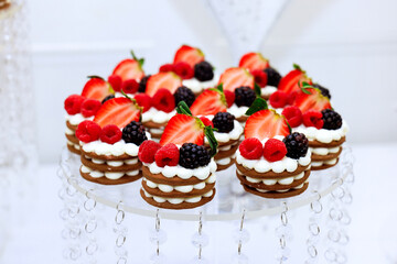 Beautiful display of layered desserts sits on decorative stand, featuring whipped cream an array of fresh strawberries, raspberries, blackberries, perfect for festive occasion.