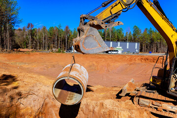 Large excavator is lifting concrete pipe to be placed at construction site to installing drainage...