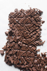 Overhead view of chopped dark chocolate on a white granite countertop, top view of dark chocolate chunks for baking