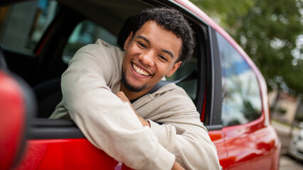 Obraz premium Young man smiling in red car with open window