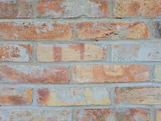 Fototapeta premium close-up of a rustic brick wall with varying shades of red, orange, and beige. The texture and uneven coloration give a vintage, weathered look, showcasing the character of aged masonry