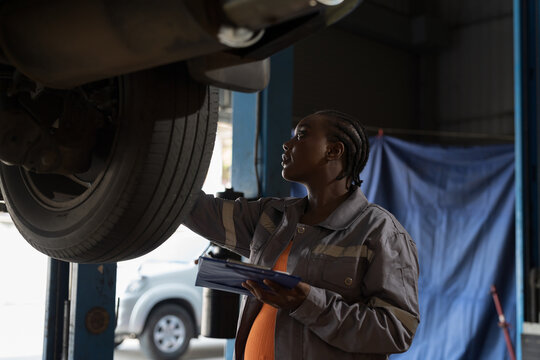 Female mechanic working at garage. Female mechanics checking tire wheel underneath lifted car at auto car repair service. Car service and Maintenance concept