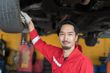 Male mechanic maintenance car engine at garage. Asian male mechanics repairing car engine underneath lifted car at auto car repair service