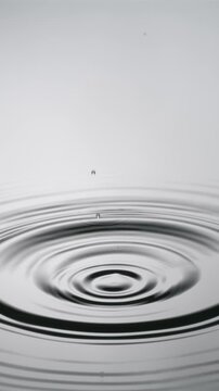 A single drop of water falling into a pool of water in slow motion. Vertical Video.