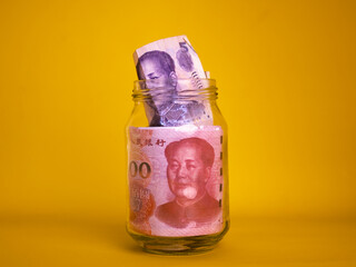 Chinese Yuan Renminbi notes in clear transparent glass jar bottle container isolated yellow background. savings concept