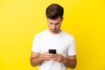 Young caucasian handsome man isolated on yellow background using mobile phone