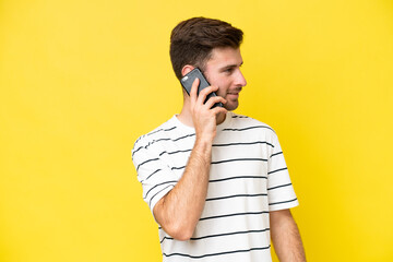 Young caucasian man isolated on yellow background keeping a conversation with the mobile phone with someone