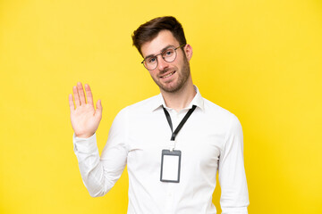 Young caucasian with ID card isolated on yellow background saluting with hand with happy expression