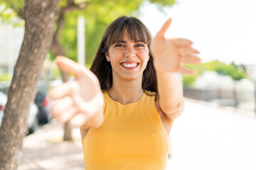 Young woman at outdoors presenting and inviting to come with hand