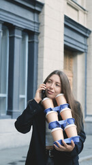 Fototapeta premium A cute woman with long hair in an office black jacket carries many glasses of takeaway coffee in her hands and talks on her smartphone.