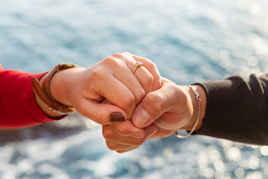 Manos entrelazadas con un anillo y el mar de fondo