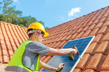Solar energy installation: a worker in a yellow hard hat and vest uses a drill to secure a solar...