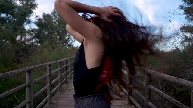 Chica joven de perfil recreando conceptos de tristeza, llorando, sufrimiento, desesperaci&oacute;n y otros., en un puente de madera en medio del bosque un d&iacute;a de verano al atardecer con cielo azul y nubes.