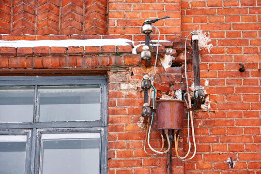  Old electrical wiring, aged exterior transformer with exposed wires and insulation on red brick building, outdated power distribution systems. Aging infrastructure, need for modern utility upgrades
