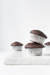 Homemade double chocolate muffins in white liners on a white countertop, dark chocolate muffins...
