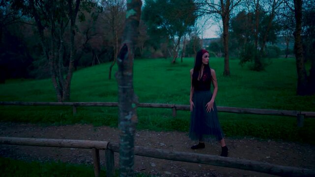 Chica joven caminando con miedo por un sendero en el bosque al caer la noche porque se cree que la siguen o vigilan.