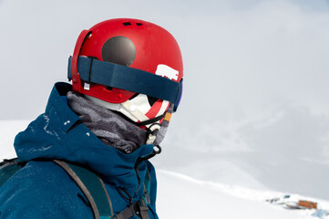 Cheerful and happy man in warm blue jacket, ski mask and helmet looking away, spending extreme weekend in winter season in mountains. Portrait of sporty guy