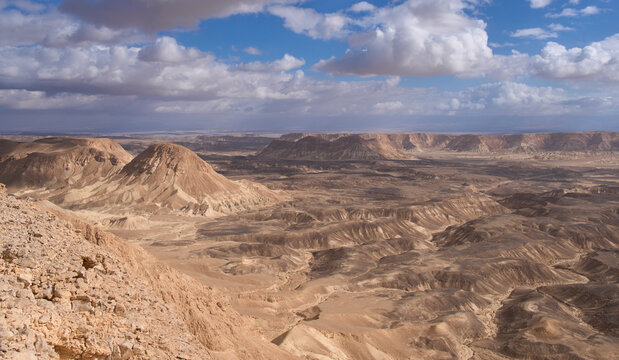 Panoramic view of fascinating and dramatic landscapes of Nahal Ashosh Nature Reserve, Negev Desert. Majestic mountain landscape. Orange sandstone mountains and hills. White clouds in the blue sky.
