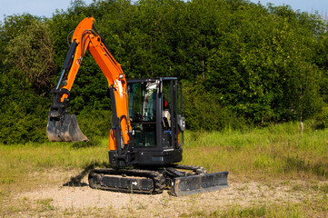 Excavator on a construction site next to a blooming field. Field with green grass and a small crawler excavator standing nearby