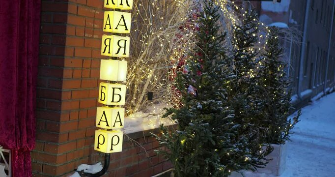 Holiday season. Christmas trees beautifully decorated with burning garlands stand in front of the showcase and the glowing inscription BAR. The camera rotates. Siberia.