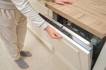 Person opening dishwasher in a modern kitchen with wooden countertop. Home appliance usage and...