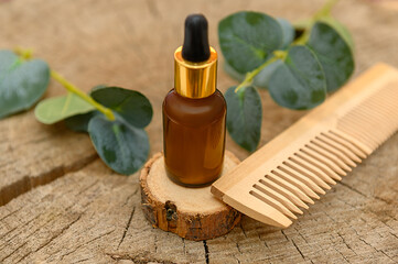 Cosmetic oil on a wooden background. With green eucalyptus branches. And a wooden comb.