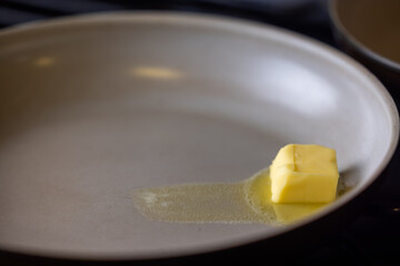 A pan with a piece of butter on it. The butter is melting and spreading out on the pan