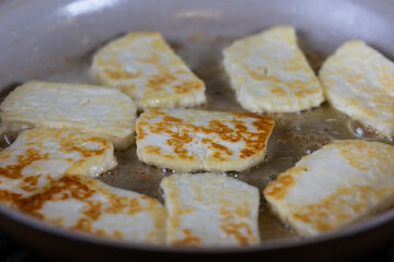 A pan of fried halloumi cheese is shown with a golden brown crust. cooking in hot butter. The dish looks delicious and inviting