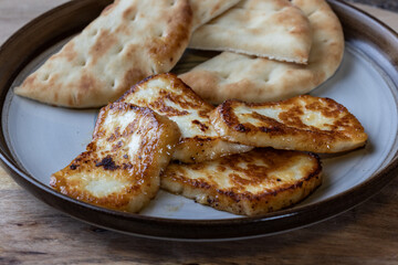 A plate of fried halloumi cheese with a side of pita bread. The food is golden brown and looks delicious.