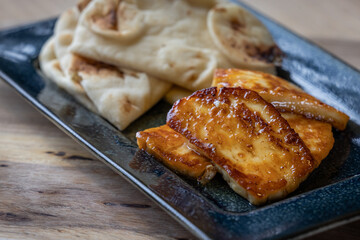 A plate of fried halloumi cheese with a side of pita bread. The food is golden brown and looks delicious.
