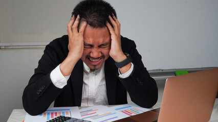 Asian business man is stressed and frustrated analyzing his financial results. On the table there...