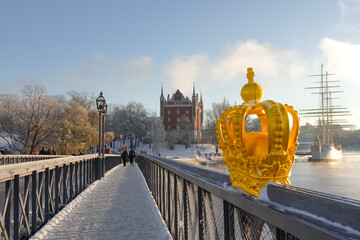 Golden crown ornament on skeppsbron bridge to skeppsholmen island bridge in central Stockholm, Sweden in winter with snow on the ground on a sunny day