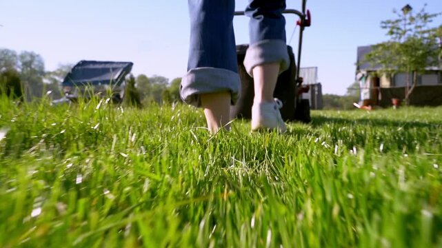 Woman with a lawnmower mows the lawn at the dacha