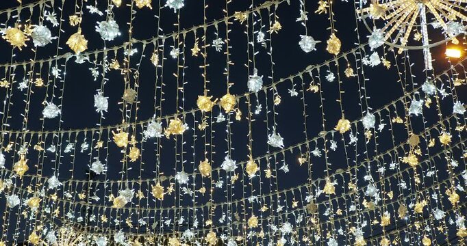 Holiday season. Many beautiful colorful garlands are hung above the street and glow in the dark, illuminating the sidewalk. The camera rotates. Hand held. Siberia.