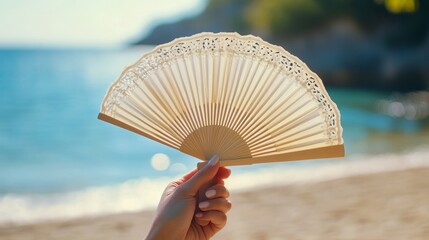 Hand Holding a Delicate Fan Against a Serene Beach Backdrop During a Sunny Day at the Coast, Capturing a Moment of Relaxation and Elegance